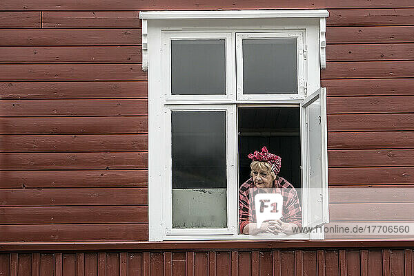 Eine Darstellerin schaut aus dem Fenster des Heringsmuseums in Siglufjorour  einem ehemaligen Fischerdorf  das heute Touristen anlockt; Siglufjorour  Island