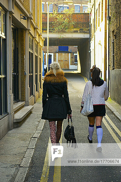 Zwei junge Frauen gehen eine schmale Straße zwischen Gebäuden entlang  Brick Lane; London  England