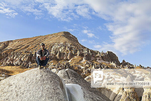 A Man Crouches On A Large Rock In A Landscape Of Fairy Chimneys; Cappadocia  Turkey