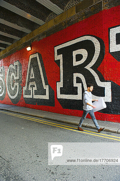 Ein Fußgänger geht auf der Straße entlang einer Wand mit großen Schriftzügen gemalt auf  Shoreditch; London  England