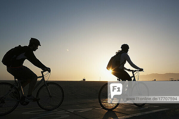 Silhouette Of Cyclists Riding On The Promenade Beside The Beach At Sunset; California  United States Of America