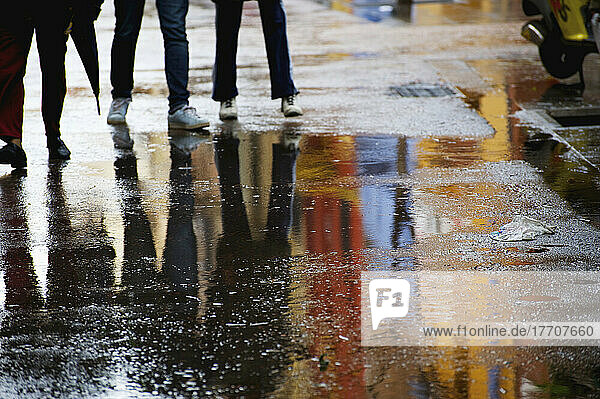 Fußgänger auf einem nassen Gehweg mit Pfützen  in denen sich die bunten Gebäude spiegeln; Barcelona  Spanien