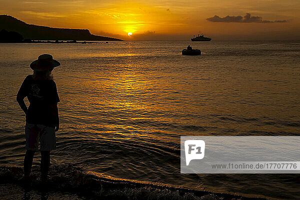 Silhouetted tourist on beach at sunset. Endeavour ship at anchor.
