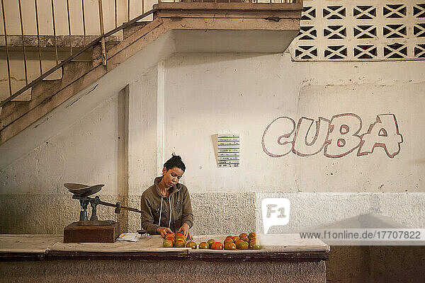 Eine Frau kümmert sich um Äpfel an einem Stand auf einem Bauernmarkt mit kubanischem Graffiti an der Wand; Cienfuegos  Kuba.