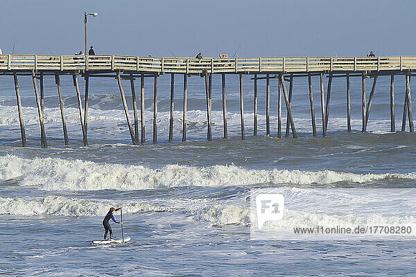 An 11 year old boy paddles out into big waves on his standup paddle board next to Nags Head pier.; Nags Head  North Carolina.