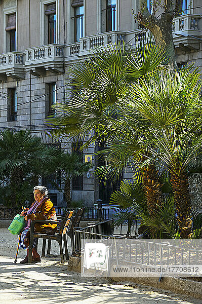 Eine ältere Frau sitzt auf einem Stuhl außerhalb eines Wohngebäudes; Barcelona  Spanien