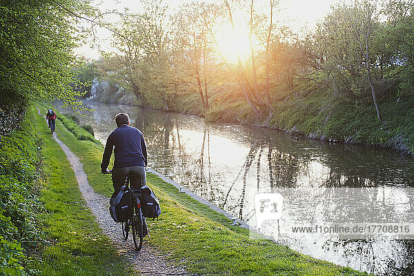 Radfahrer  der bei Sonnenuntergang entlang des Kanals radelt; Wiltshire  England