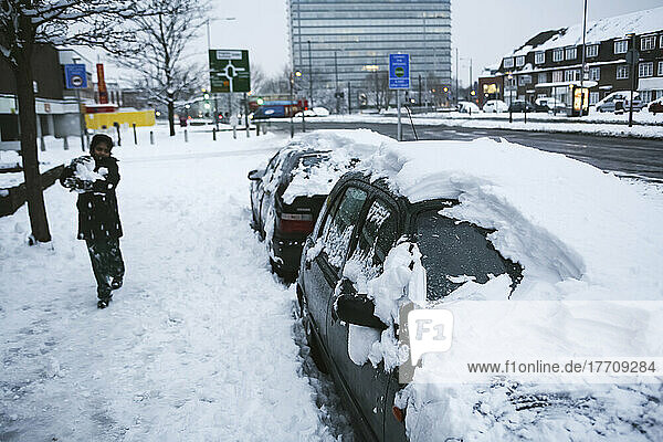 Entfernen eines Teils des tiefen Schnees von schneebedeckten Autos  um einen Schneemann zu bauen  mit dem Tolworth Tower im Hintergrund; London  England