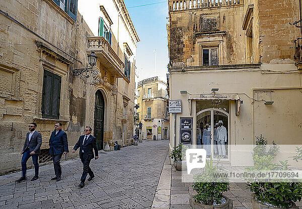 Drei Männer spazieren auf dem Stadtplatz vorbei an Geschäften im historischen Zentrum von Lecce  Italien; Lecce  Apulien  Italien