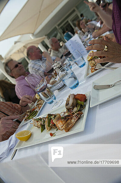 Ein Tisch mit Touristen  die ein Mittagessen im Freien mit aufgespießten Meeresfrüchten genießen; Djerba  Tunesien