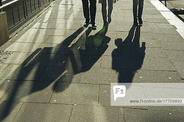 Fußgänger und ihr Schattenwurf auf dem Bürgersteig bei Sonnenaufgang; Hamburg  Deutschland