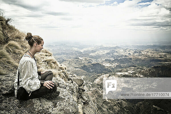 Eine junge Frau sitzt auf einem Bergrücken mit Blick auf die spektakulären Simien-Berge; Äthiopien