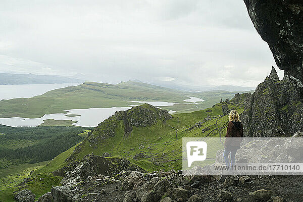 Eine Frau steht auf einem felsigen Bergrücken und blickt auf die Landschaft mit Hügeln und Wasser; Skye  Schottland