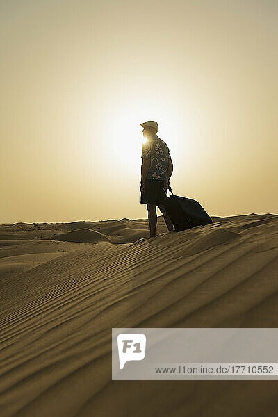 Barfuß Mann mit Koffer auf Sanddüne in der Abenddämmerung; Dubai  Vereinigte Arabische Emirate