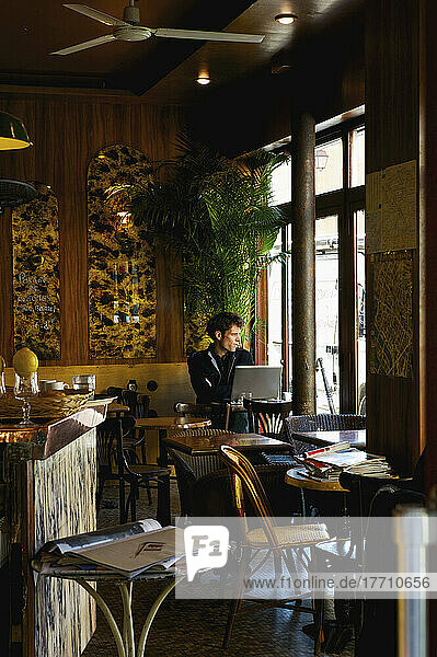 Ein Mann sitzt an einem Tisch in einem Café mit seinem Laptop-Computer und starrt aus dem Fenster  Bezirk Marais; Paris  Frankreich