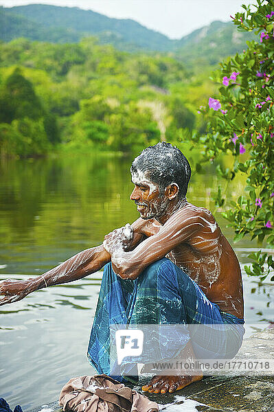 Ein junger Mann hockt am Rande des Wassers  bedeckt mit Seifenlauge; Ulpotha  Embogama  Sri Lanka