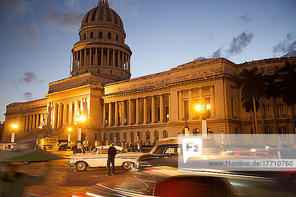In der Abenddämmerung erhellen Lichter vor dem El Capitolio-Gebäude eine Straße  die mit amerikanischen Oldtimern gefüllt ist; Havanna  Kuba