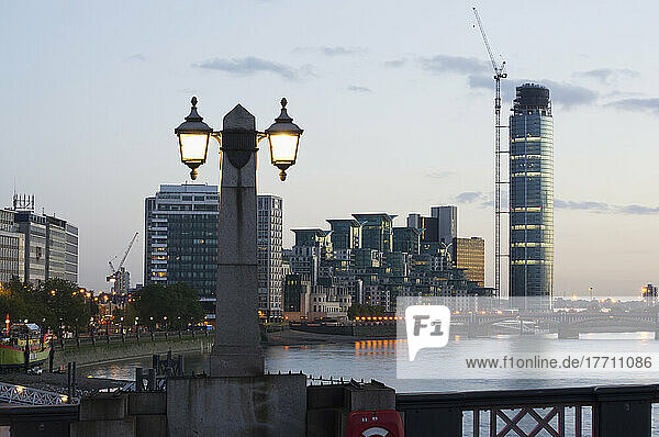 In der Dämmerung beleuchteter Laternenpfahl und Gebäude entlang der Waterfront; London  England