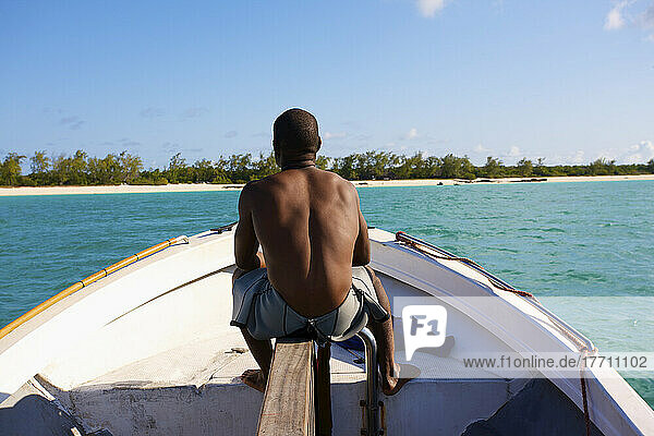 Ein Mann sitzt auf seinem Boot auf dem ruhigen türkisfarbenen Indischen Ozean mit Blick auf den weißen Sandstrand; Vamizi Island  Mosambik