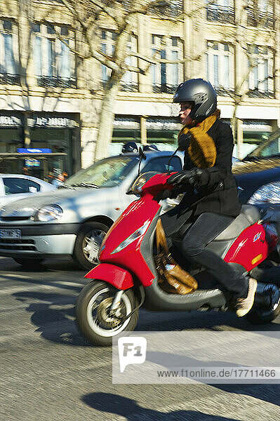 Eine Frau fährt mit ihrem motorisierten Roller die Straße entlang; Paris  Frankreich