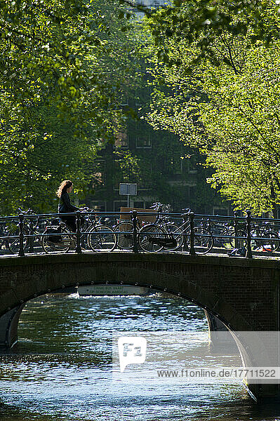Frau auf Fahrrad überquert Brücke früh am Morgen; Amsterdam  Holland