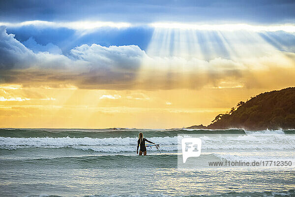 Ein wunderschöner Sonnenaufgang begrüßt eine Surferin  die sich auf das Surfen am frühen Morgen vorbereitet und hinauspaddelt; Arrawarra  New South Wales  Australien