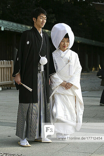 After The Traditional Japanese Shinto Wedding Ceremony Families Gather For A Formal Portrait Sitting  At Meiji Jingu Shrine; Near Harajuku Station; Tokyo. Here The Bride And Groom Pose For A More Informal Shot After The Formal Photo Sitting.There Are Several Layers Of The Brides White Kimono And A Silk Brocade Covers All. Traditionally The Bride Will Be Completely Covered From Head To Toe In White As A Symbol Of Purity. A Traditional Head Covering Called A Tsuno Kakushi Literally Meaning 'to Hide Horns' Is Also Worn By The Bride  Traditionally To Signify That She Will Be A Serene And Patient Wife. The Groom's Ensemble Is Simpler  In A Traditional Shinto Wedding Ceremony He'll Wear Dark Pleated Pants  And A Short Black Kimono  Emblazoned With His Family Seal.