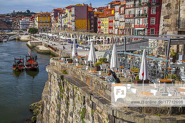 Colourful buildings along the river in Porto with a restaurant patio in the foreground; Porto  Ribeira District  Portugal
