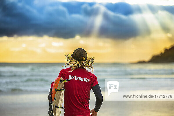 View taken from behind of a surfing instructor looking out at ocean greeted by a beautiful sunrise as he prepares to set out for an early morning surf; Arrawarra  New South Wales  Australia