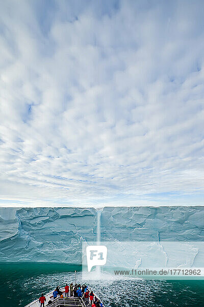 Touristen beobachten von einem Kreuzfahrtschiff aus einen Schmelzwasserfall auf einer Eiskappe.