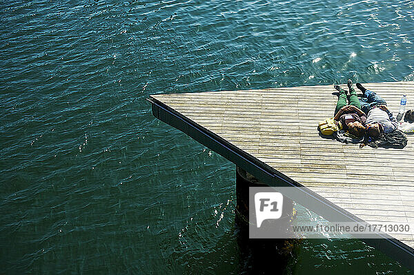 Ein Paar  das auf einem hölzernen Dock am Rande des Wassers im warmen Sonnenschein liegt; Barcelona  Spanien