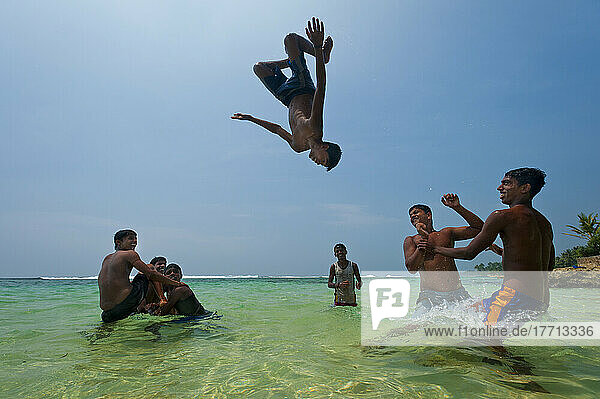 Teenager  die sich gegenseitig in die Luft werfen und Rückwärtssaltos im flachen Wasser machen  Thalpe  in der Nähe von Unawatuna; Sri Lanka