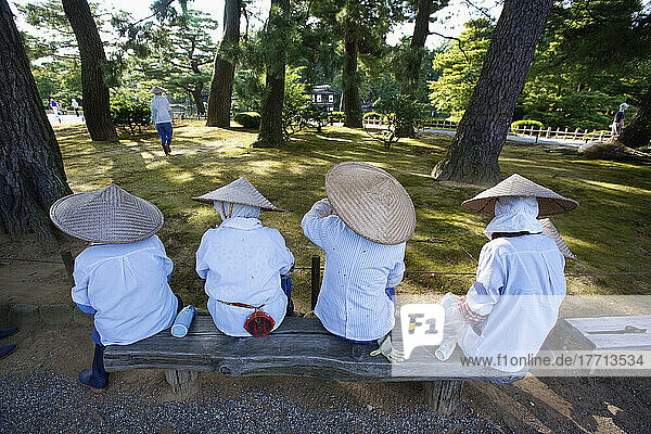 Women In Conical Hats Sitting In A Row On A Bench; Japan