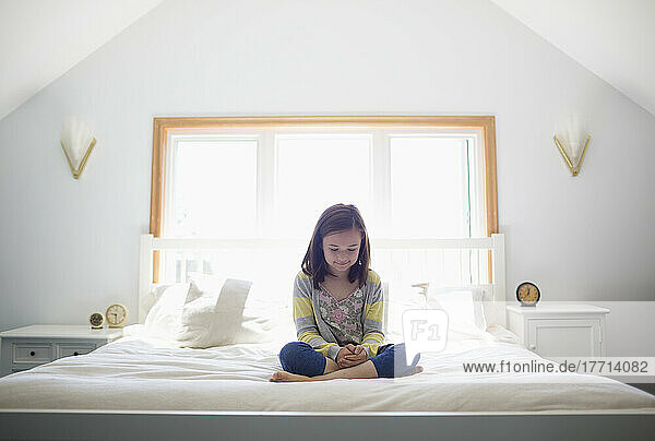 Young Girl Sitting Cross-Legged On Her Bed; Victoria  Vancouver Island  British Columbia  Canada