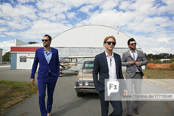 Three Businessmen Walking Away From A Car And Airplane Hangar; Langley  British Columbia  Canada