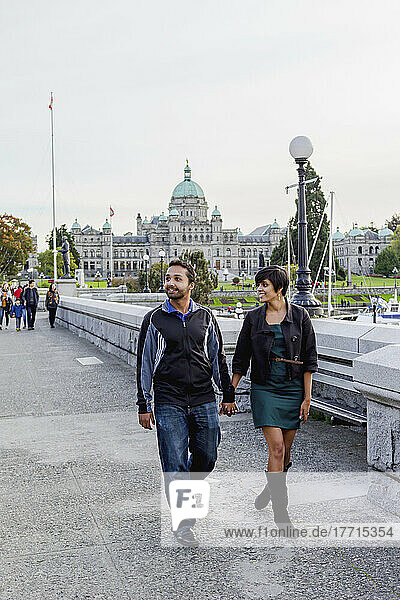 Ein junges indianisch-ethnisches Paar  das an der Uferpromenade vor den Parlamentsgebäuden spazieren geht; Victoria  Vancouver Island  British Columbia