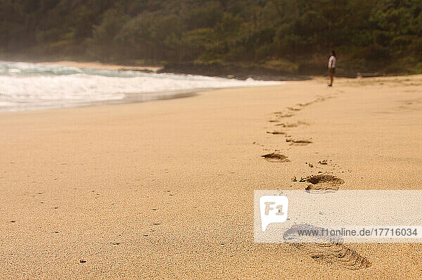 Fußabdrücke im Sand an einem Strand mit einer Frau in der Ferne