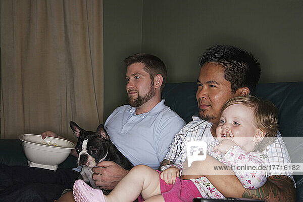 Homosexuelles Paar sitzt auf Couch mit Kind und Boston Terrier