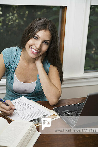 Porträt einer Frau  die an einem Tisch mit einem Laptop sitzend Papierarbeiten erledigt