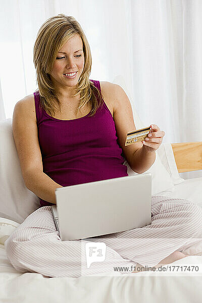 Frau auf einem Bett sitzend mit einem Laptop  der einen Online-Einkauf tätigt
