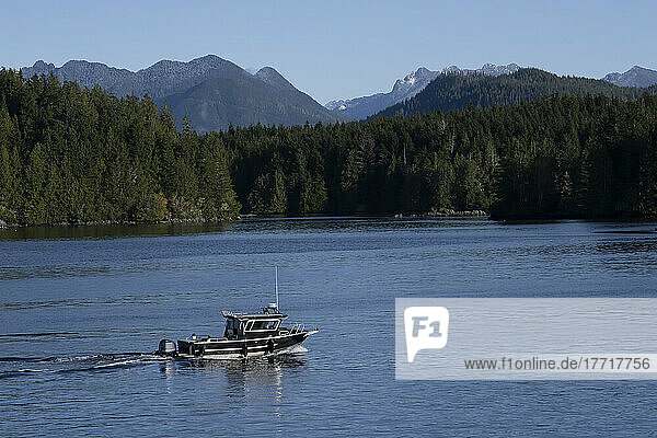 Kleines Motorboot fährt langsam entlang der Küste von Vancouver Island bei der Stadt Tofino mit Blick auf den gemäßigten Regenwald und die Coast Mountains; Tofino  British Columbia  Kanada