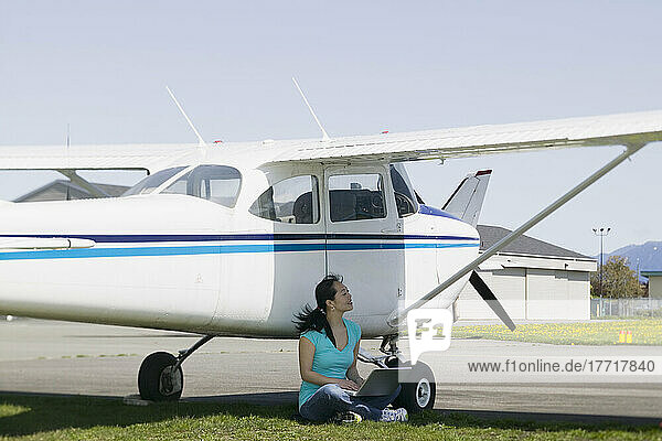 Asiatische Frau sitzt bei Cessna 172 mit einem Laptop