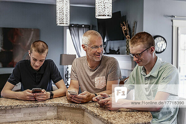Vater und zwei Söhne sitzen zu Hause an der Kücheninsel und benutzen ihre Smartphones  wobei der Vater versucht  mit ihnen zu sprechen; Edmonton  Alberta  Kanada