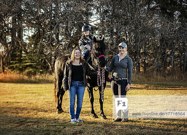 A young girl with Cerebral Palsy posing with her Mom  her trainer and a horse during a Hippotherapy session after a trail ride; Westlock  Alberta  Canada