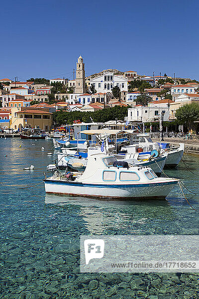 Close-up of fishing boats moored at the waterfront in Emborio Harbor with traditional buildings and the clock tower in the town center on Halki (Chalki) Island; Dodecanese Island Group  Greece