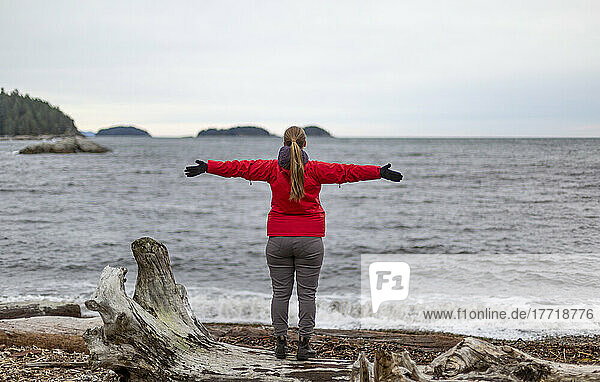 Frau steht am Ufer und blickt mit ausgestreckten Armen auf den Ozean  Sergeant Bay  Sunshine Coast; British Columbia  Kanada