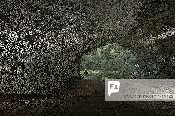Ein Mann steht am Eingang der Ignatjewskaja-Höhle im Uralgebirge und blickt auf einen Wald; Russland