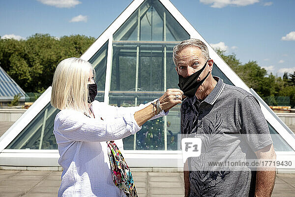 Ein älteres Ehepaar steht während der Covid-19-Pandemie mit Gesichtsmasken im Freien  wobei die Frau ihrem Mann die Maske abnimmt; Edmonton  Alberta  Kanada