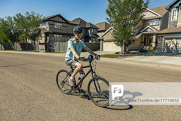 Junger Mann fährt mit dem Fahrrad eine Wohnstraße entlang; Edmonton  Alberta  Kanada