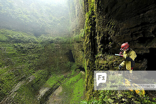 Ein Höhlenforscher auf einem kleinen Felsvorsprung mit Blick auf die riesige Bodenfläche von Niubizi Tian Keng im Er Wang Dong-Höhlensystem.